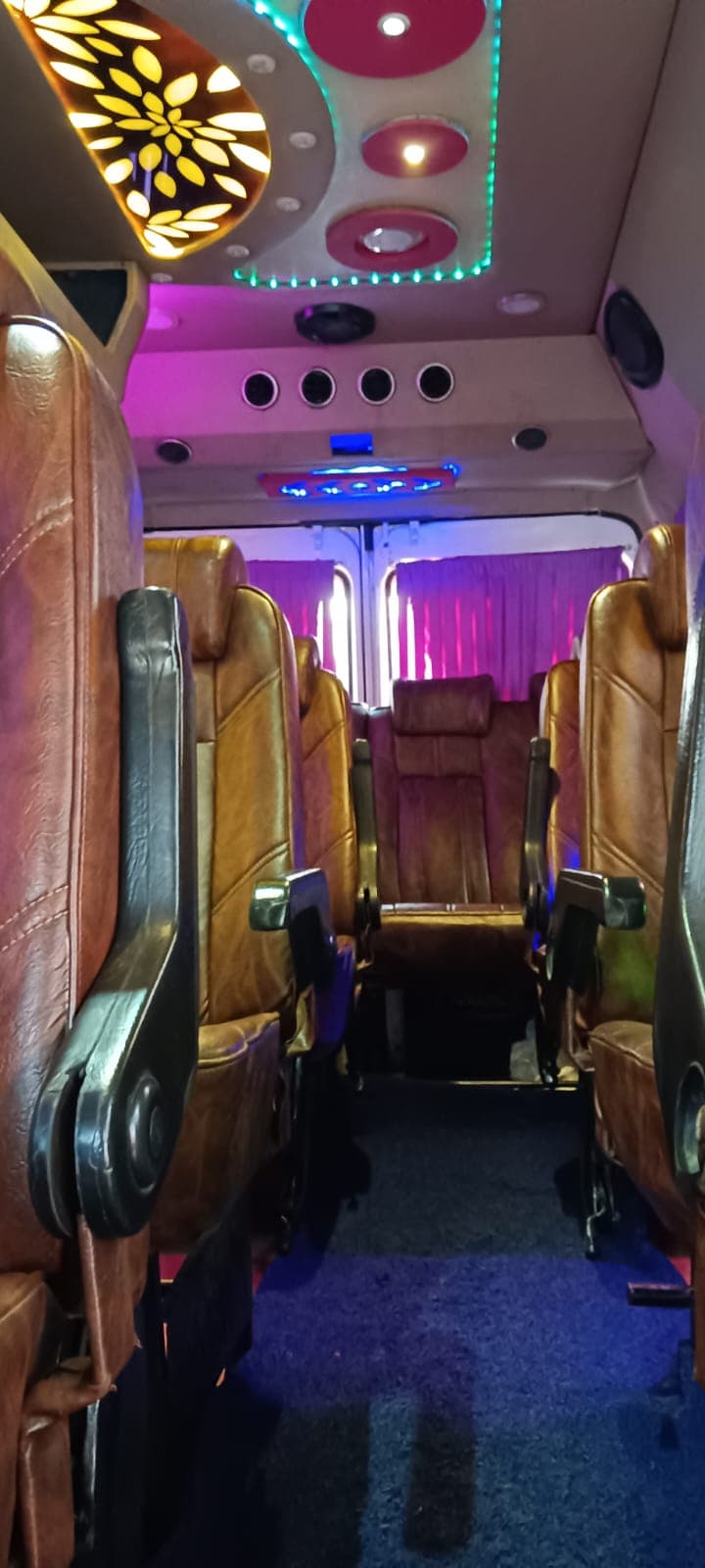 Tempo Traveller interior with tan leather recliner seats and colourful ceiling lights