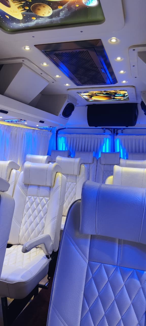 Tempo Traveller interior with white quilted seats, blue lighting and a galaxy-themed ceiling