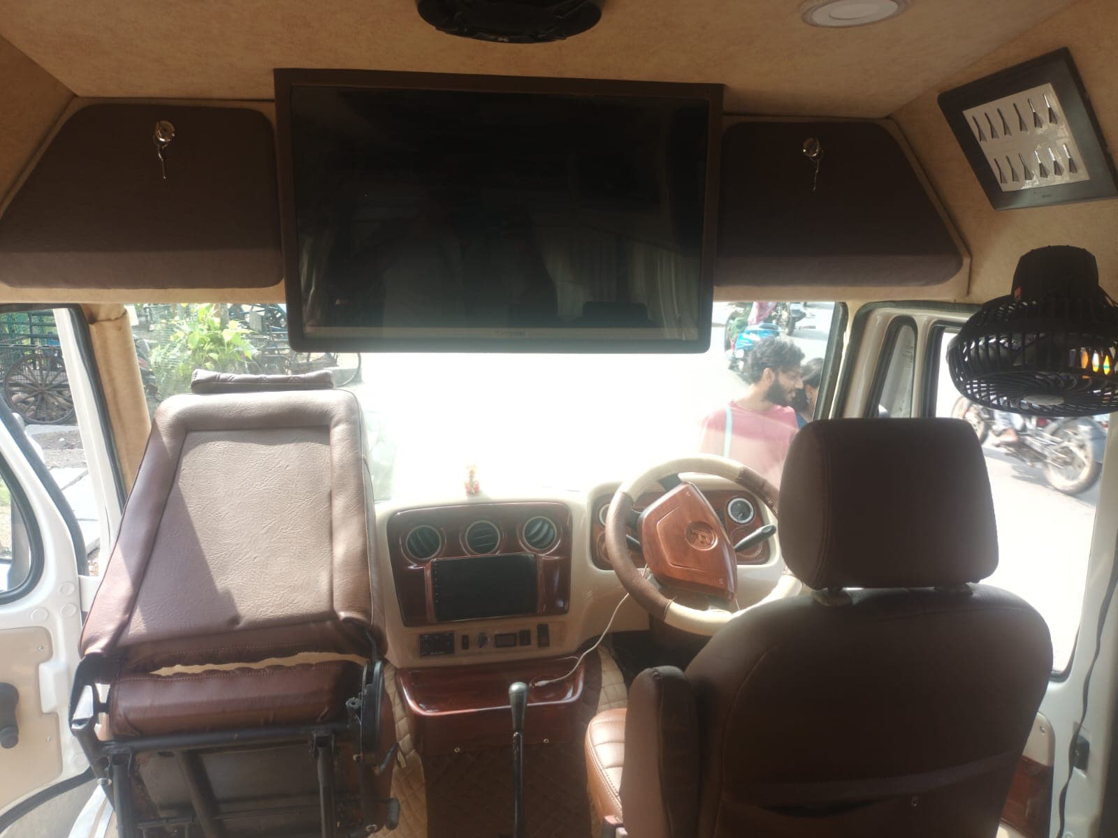 Tempo Traveller driver cabin with dashboard, wood-trim steering wheel and roof-mounted TV