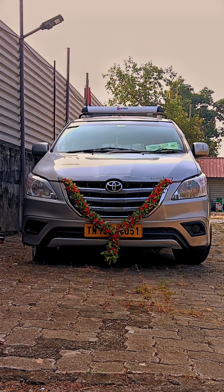 Silver Toyota Innova adorned with a fresh rose garland, front view