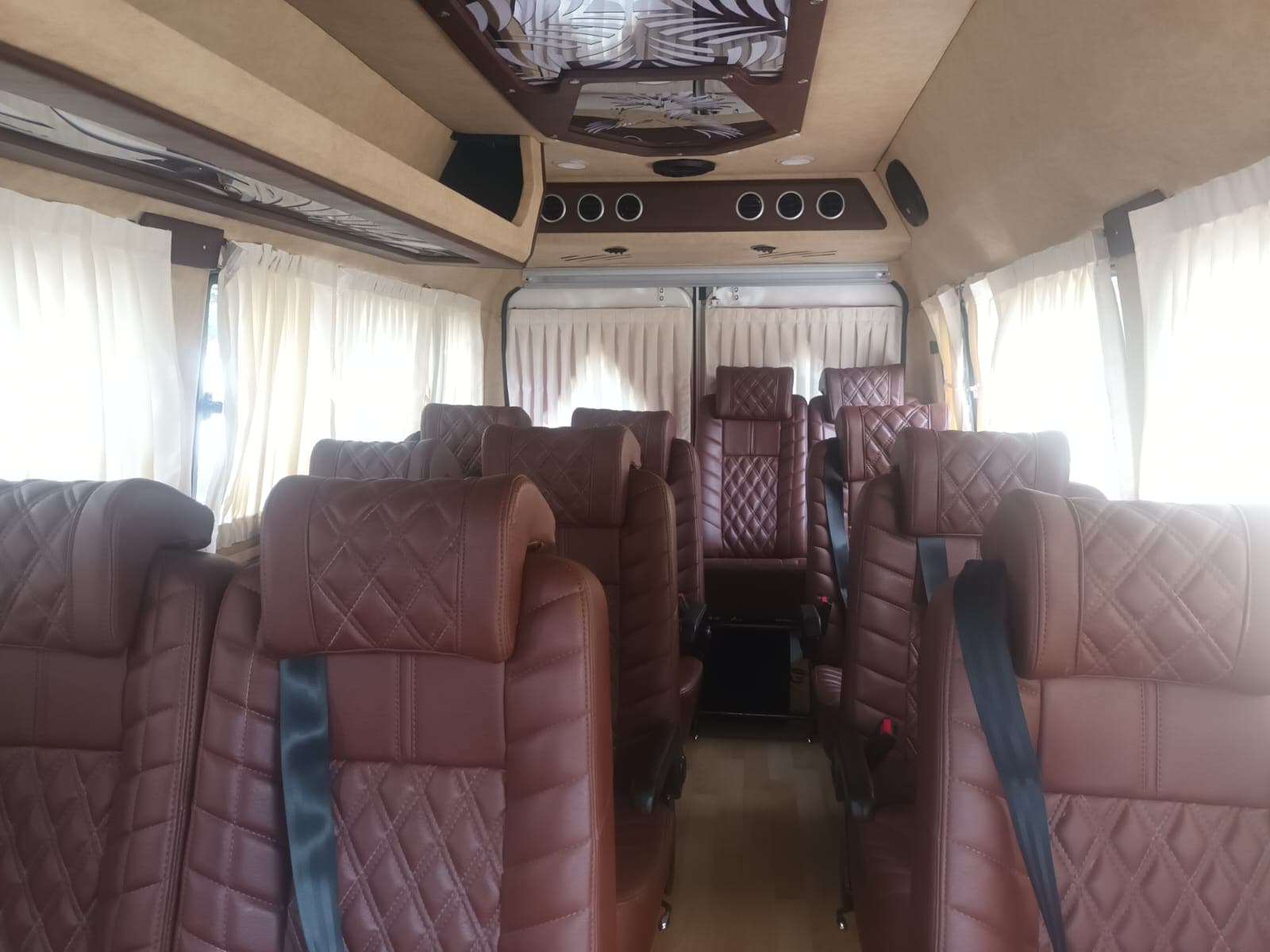 Tempo Traveller cabin with maroon quilted seats and curtained windows